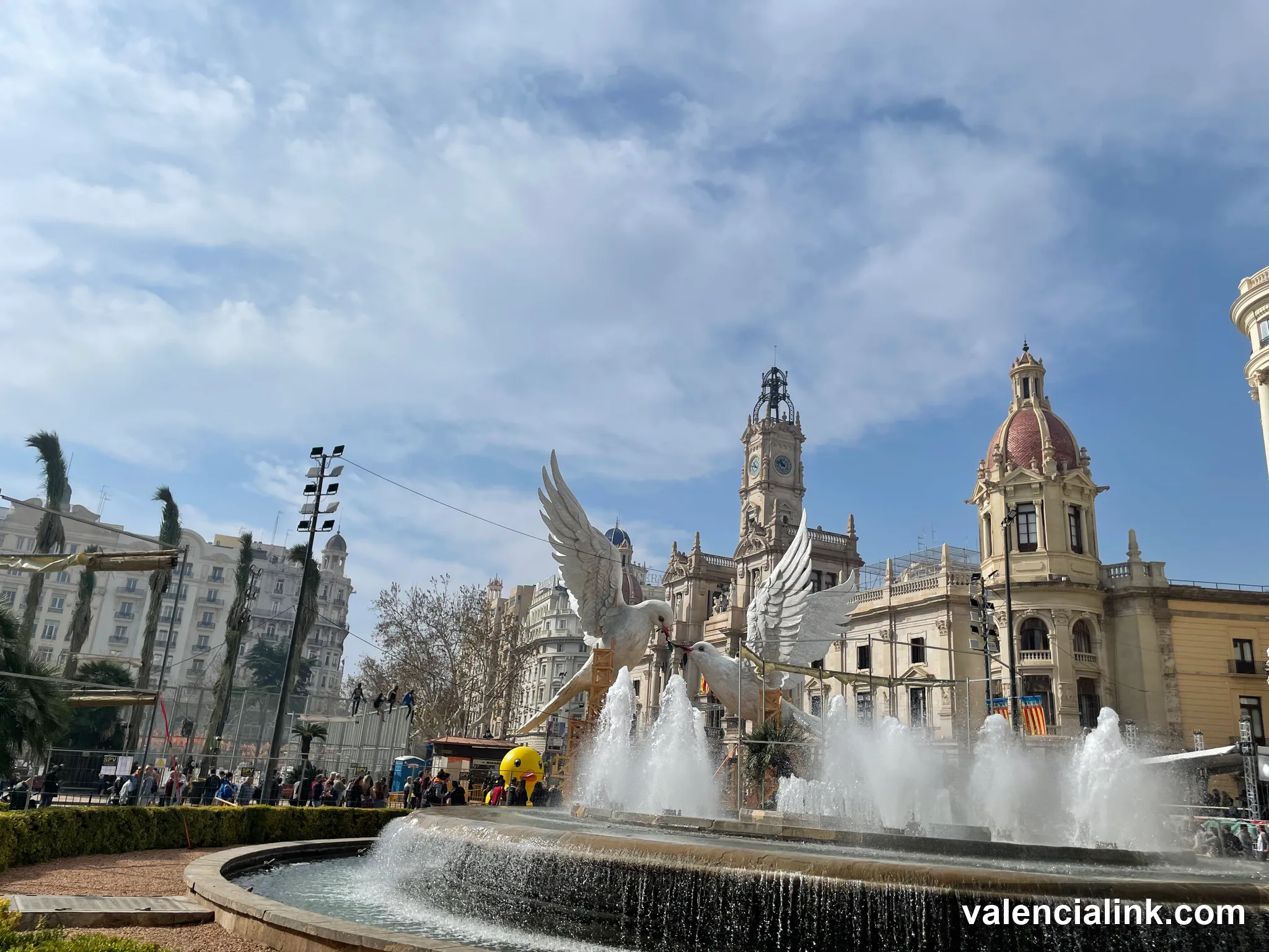 Fountain with winged statue in front of historic building with clock tower.