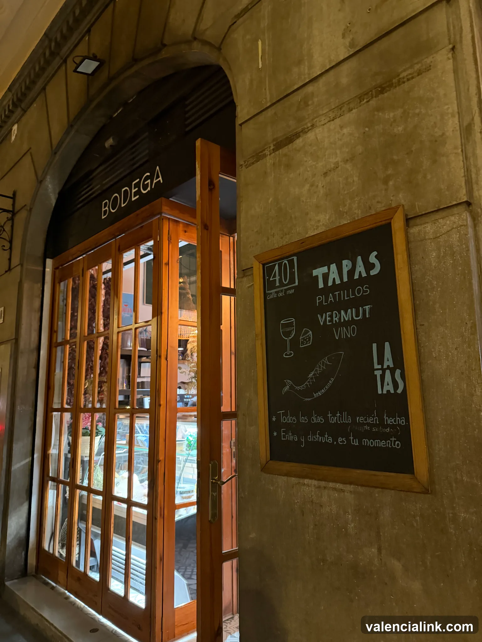 A wooden-framed door leading to a 'Bodega' with a chalkboard menu listing tapas and drinks.