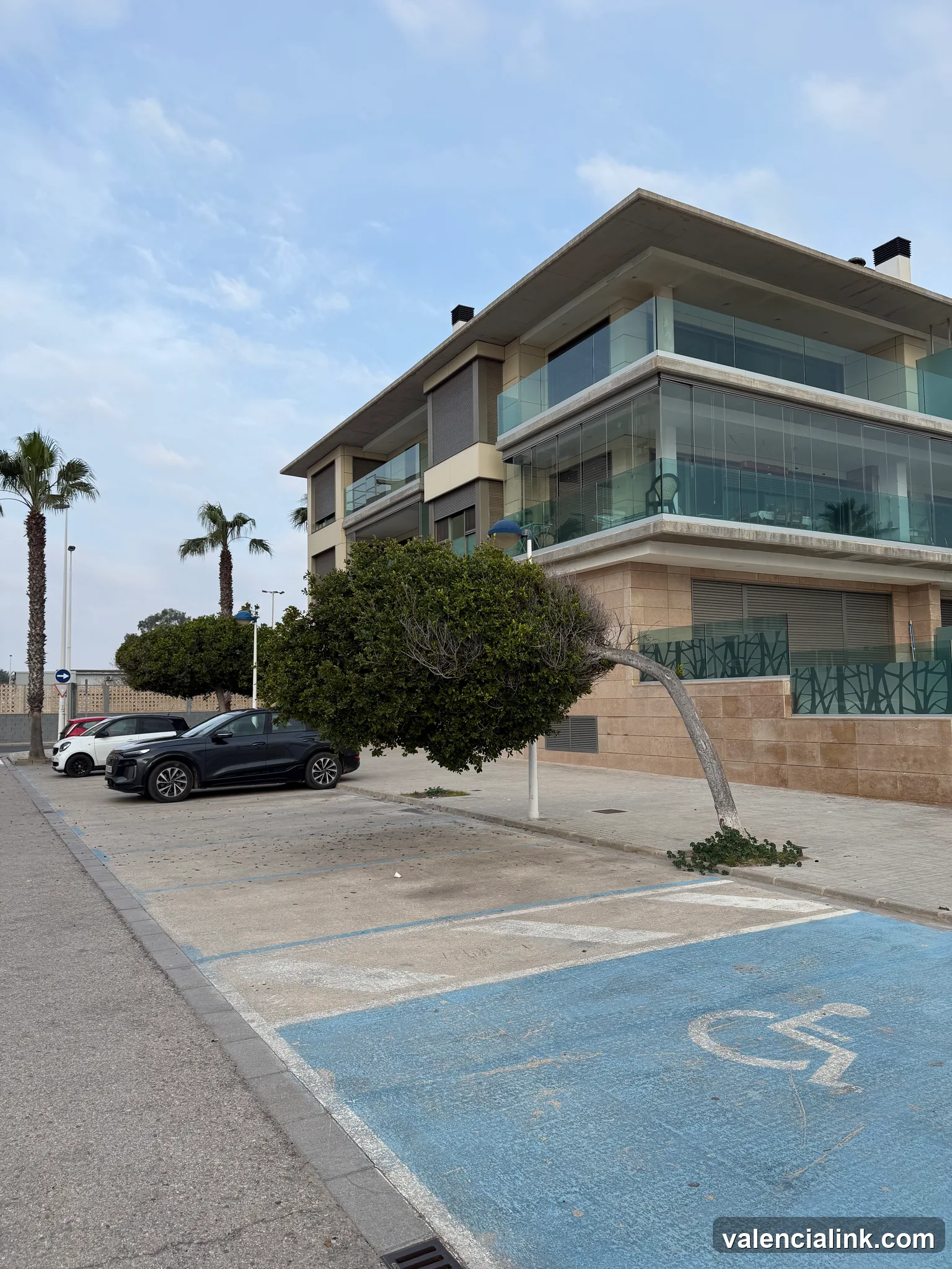 Modern building with glass balconies and a parking area marked for disabled access.