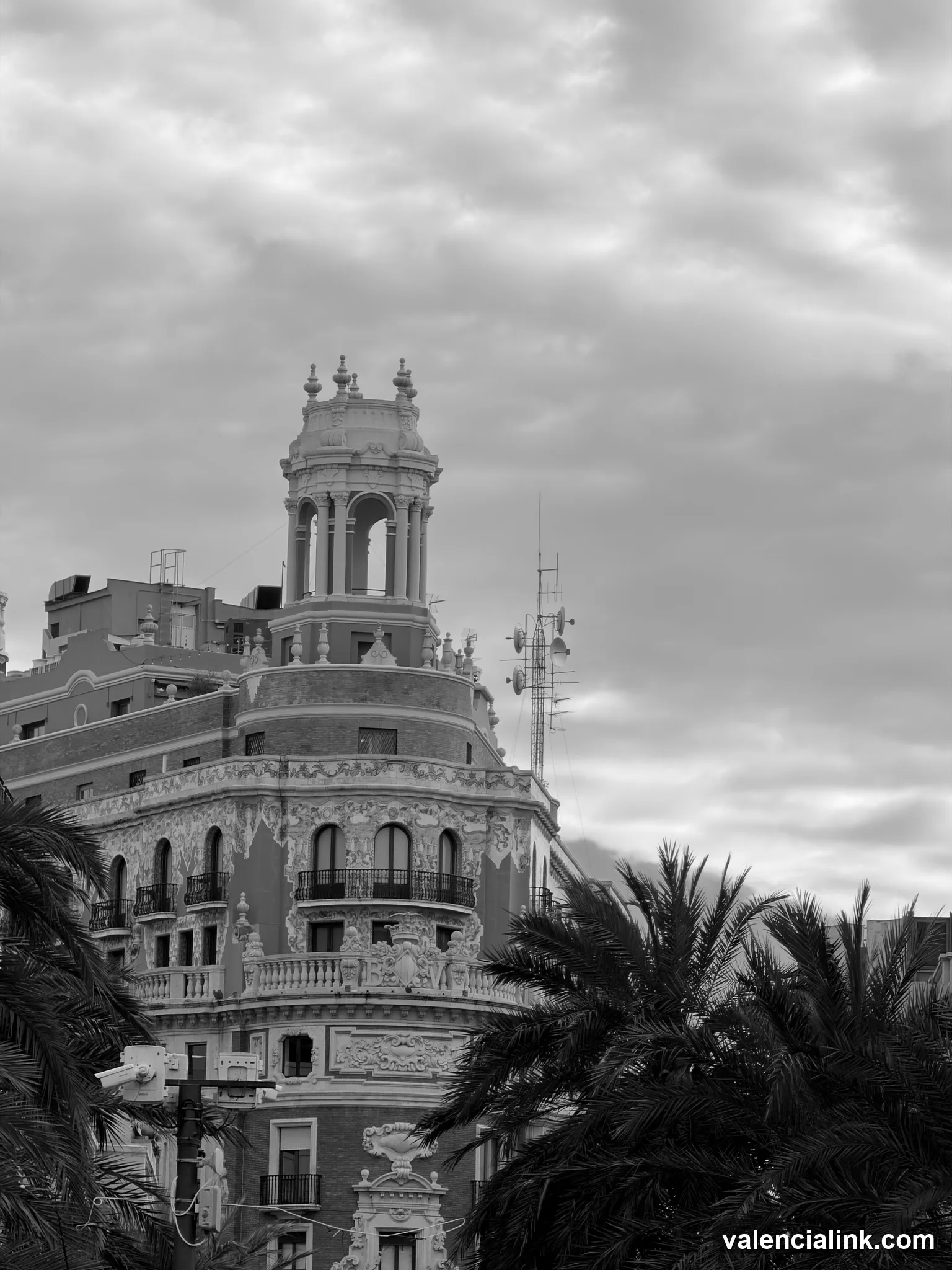 Ornate building with balconies and tower, palm trees, cloudy sky
