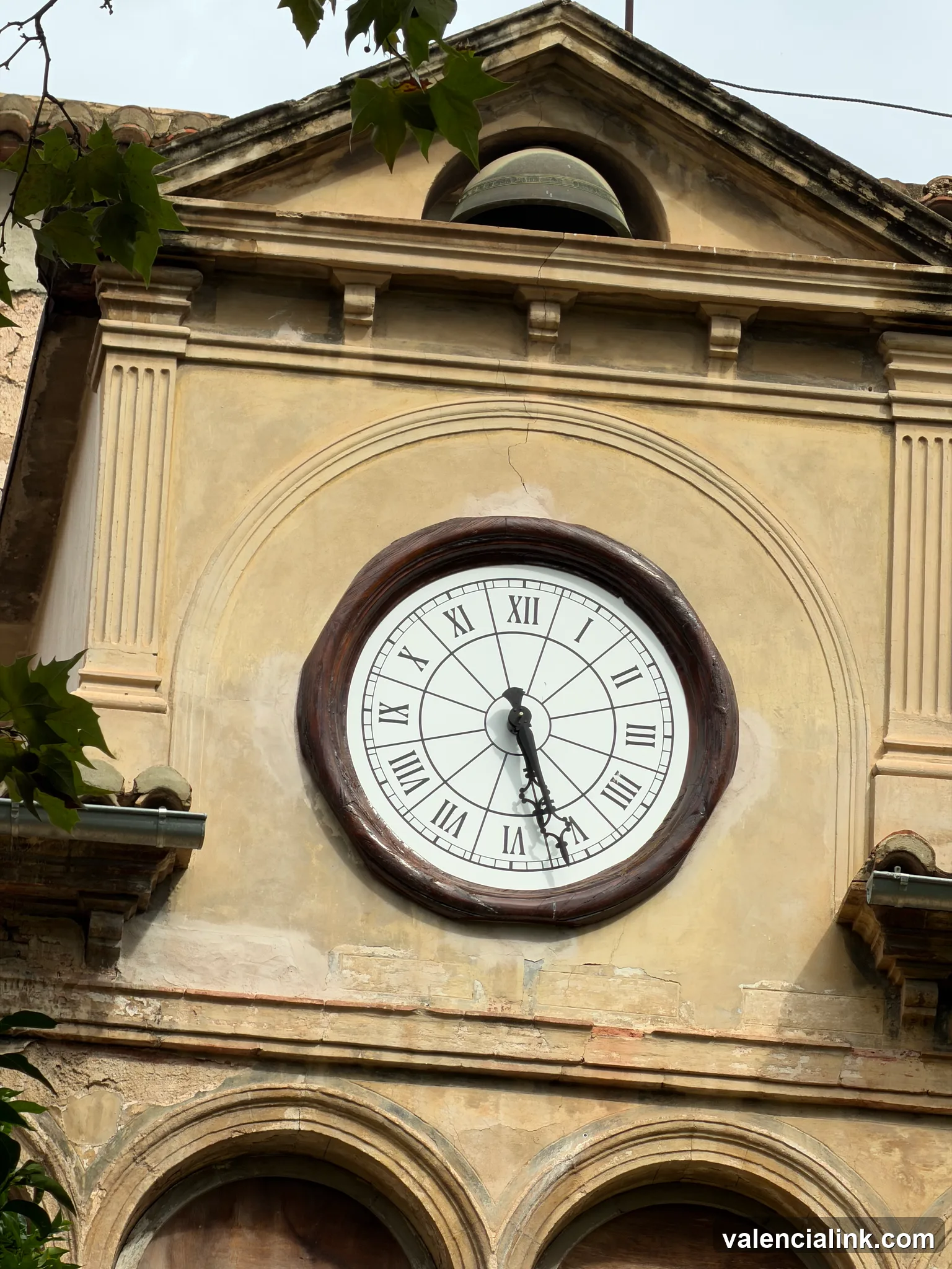 A large clock with Roman numerals on a building facade with arched windows and decorative columns.