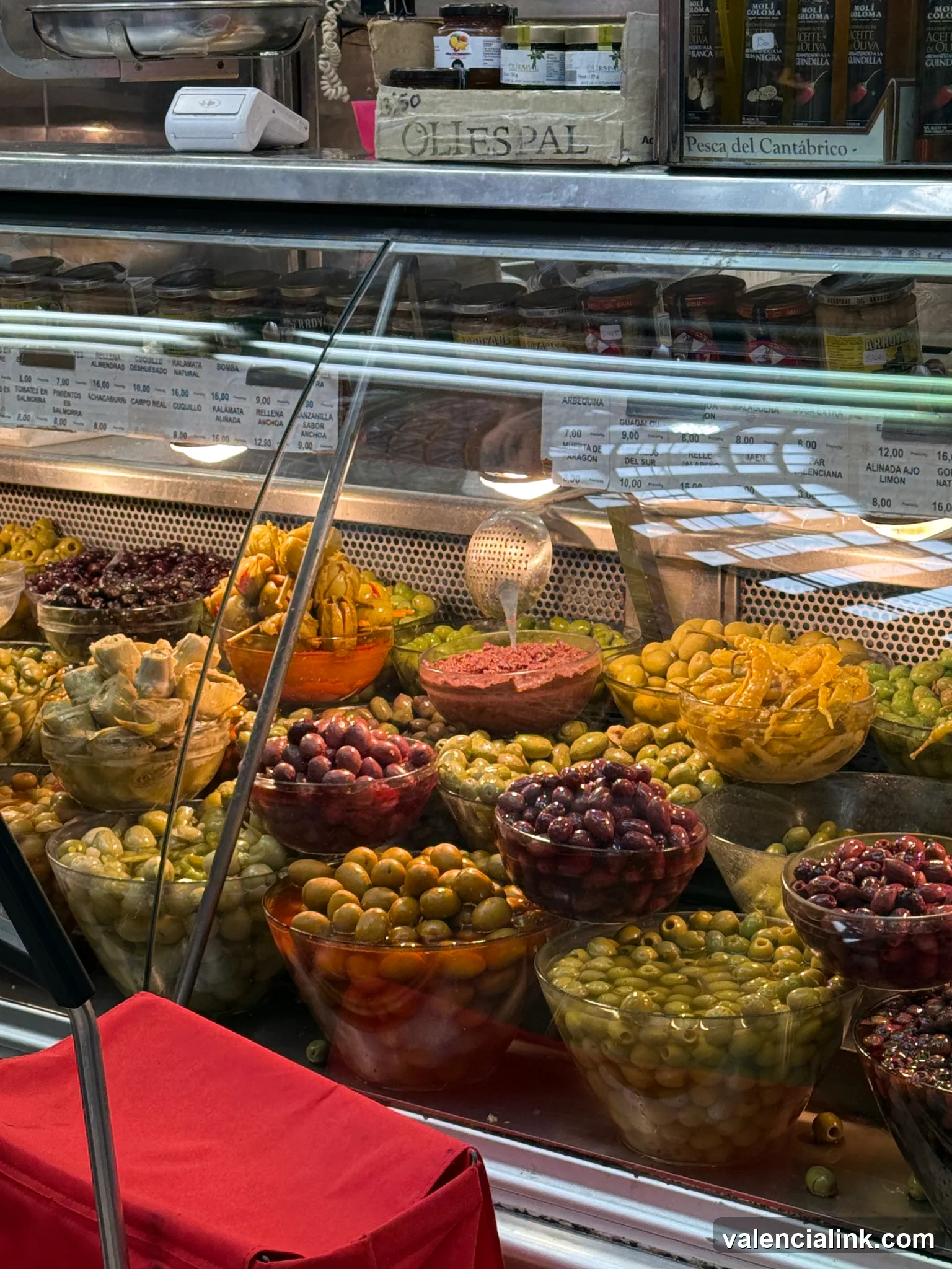 A display case filled with different types of olives and pickled items in a market setting.
