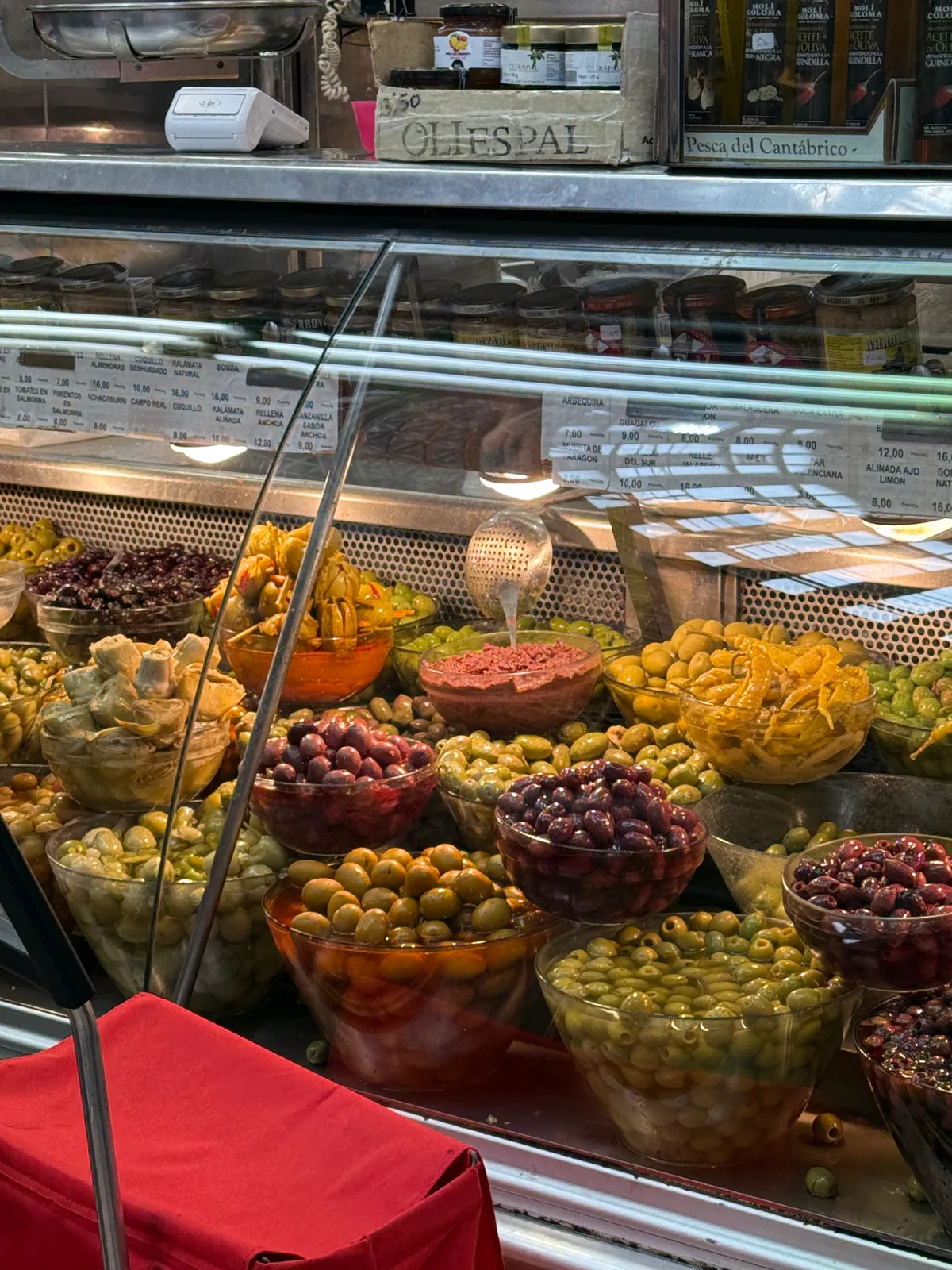 A display case filled with different types of olives and pickled items in a market setting.