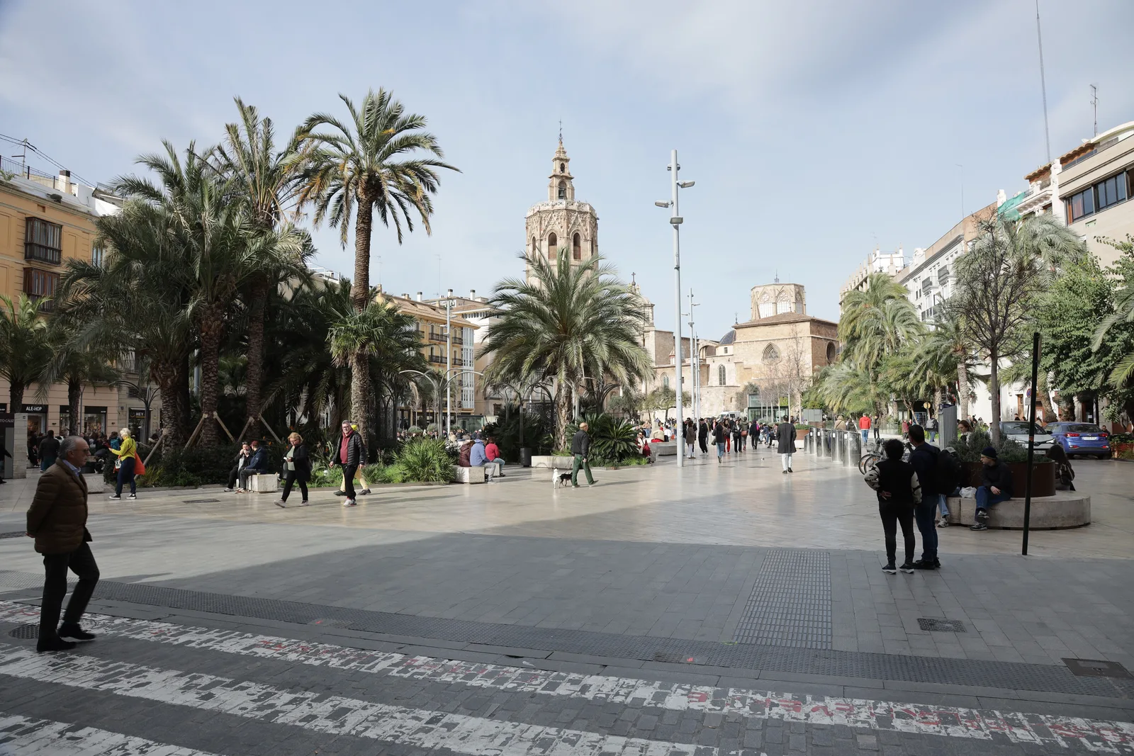 A plaza with palm trees, a church tower, and people walking in Valencia, Spain.