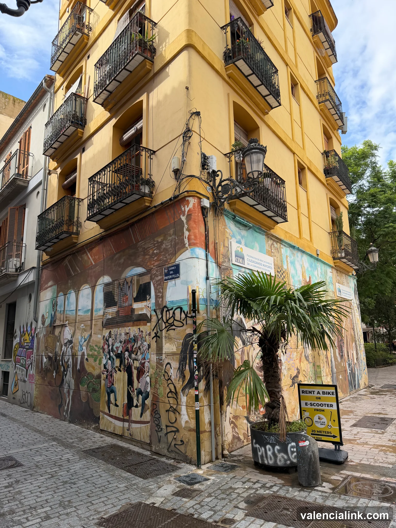 A colorful mural on a yellow building in a narrow street with cobblestone pavement.