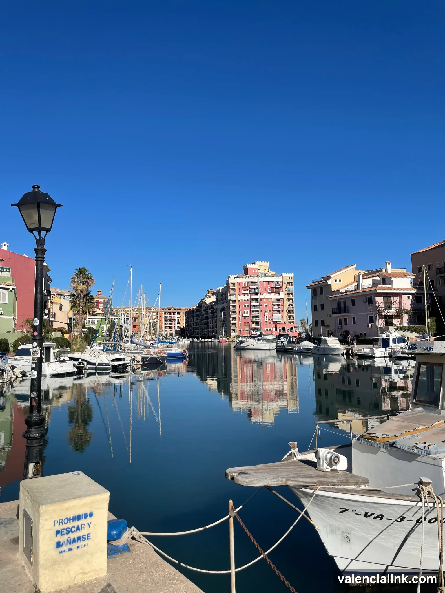 A tranquil harbor with buildings and boats under a bright blue sky.