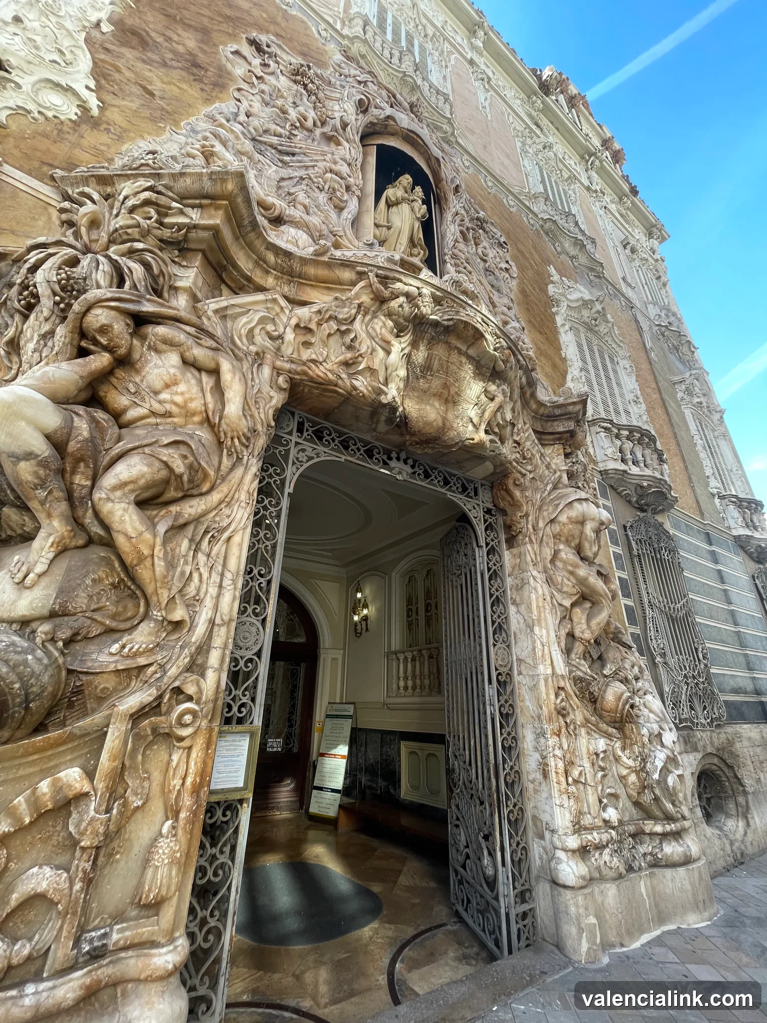 An ornate stone entrance with intricate sculptures and a decorative wrought iron gate.