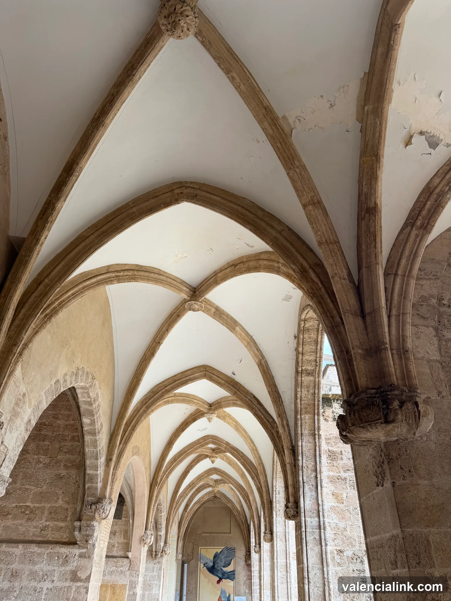 A corridor with Gothic arches and stone columns leading to a brightly lit entrance.