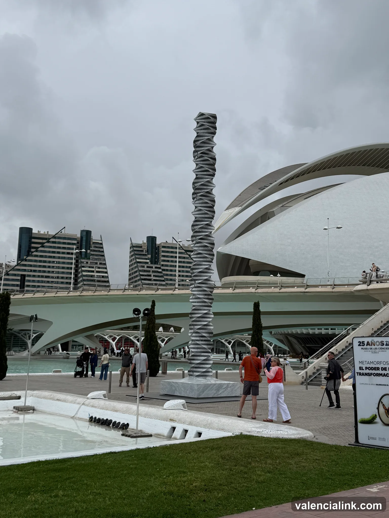Modern sculpture with people and futuristic architecture in the background.