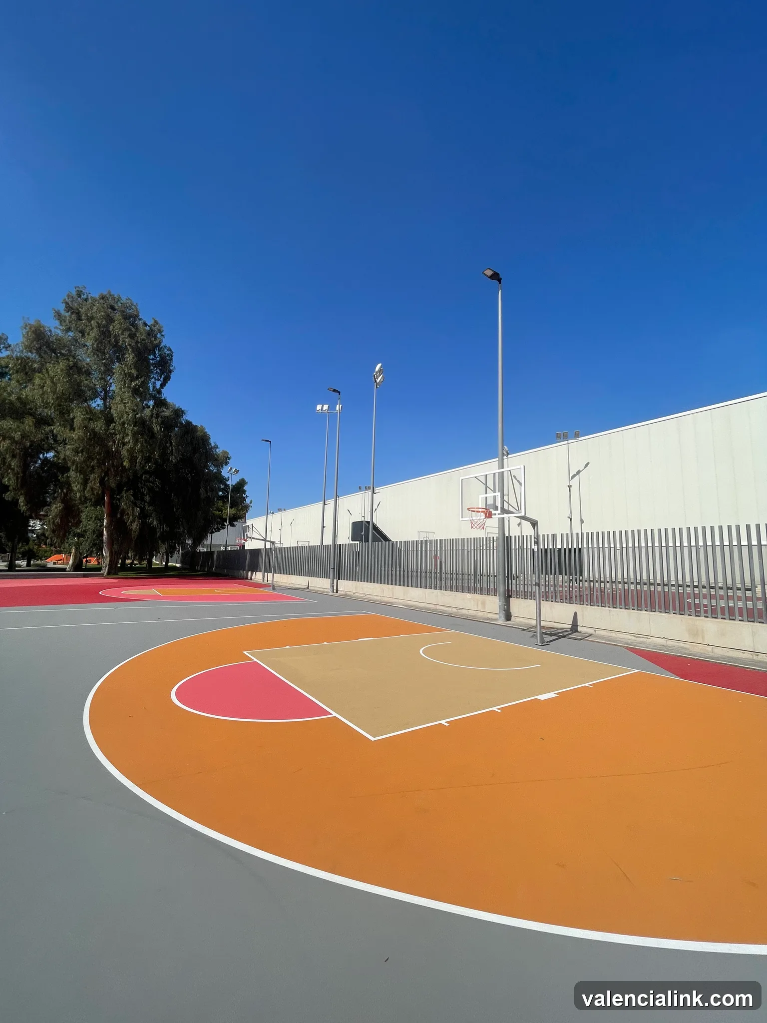 A basketball court with an orange and red design under a clear blue sky.
