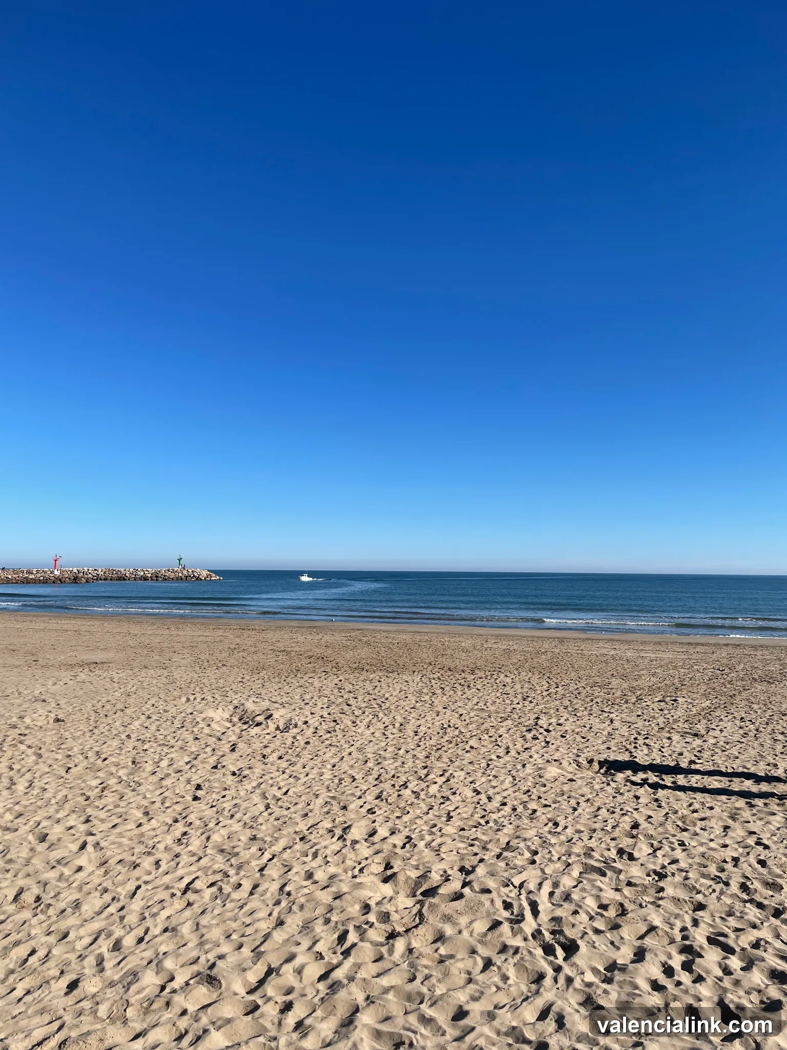 A sandy beach with a clear blue sky and a distant boat on the horizon.