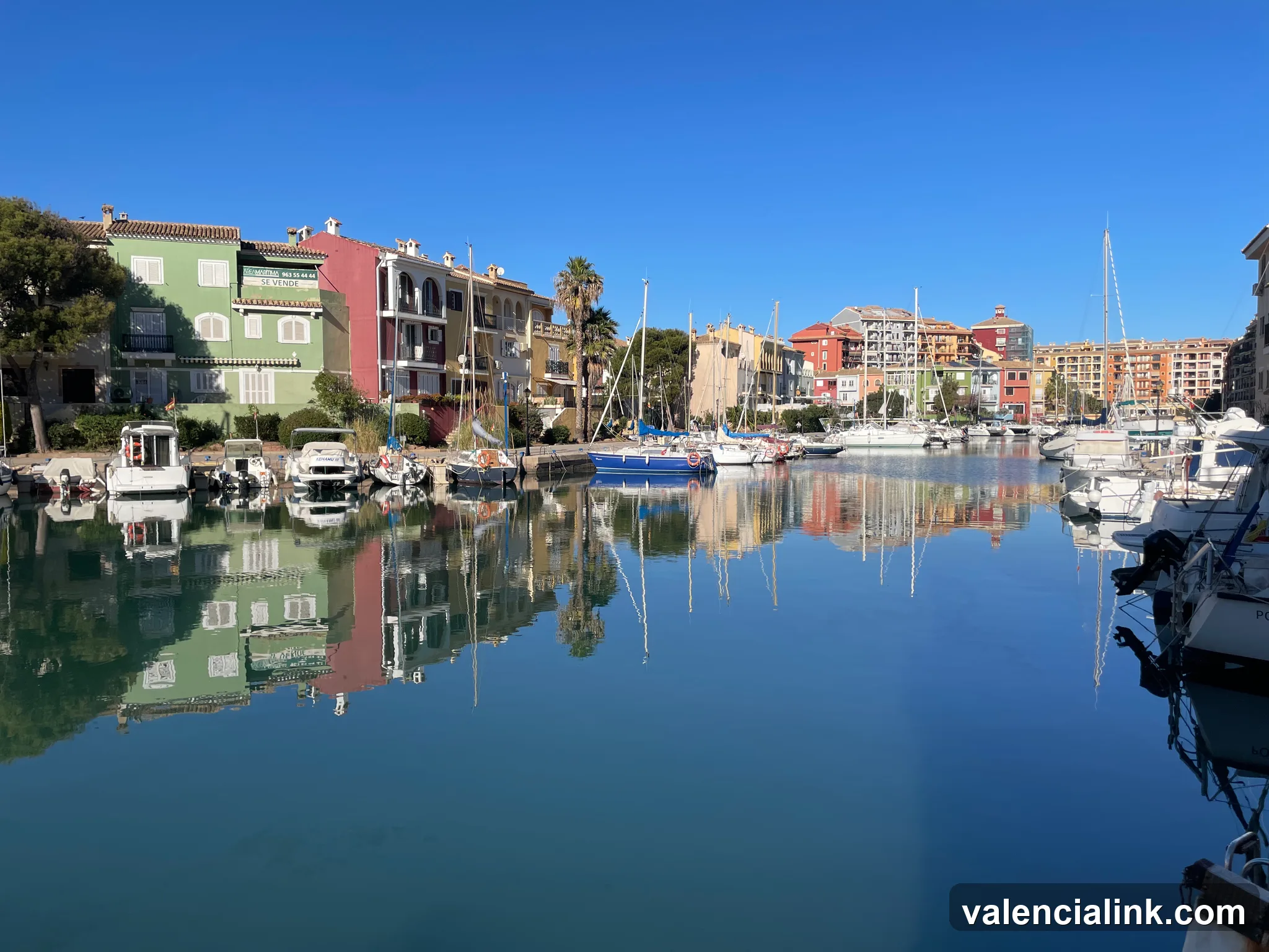 A serene marina with colorful buildings and boats reflected in still water.