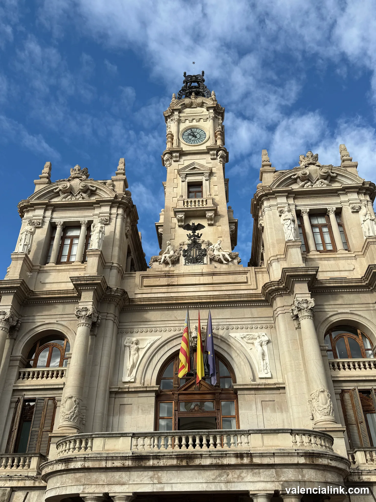 A historic stone building with intricate details and a clock tower against a blue sky.