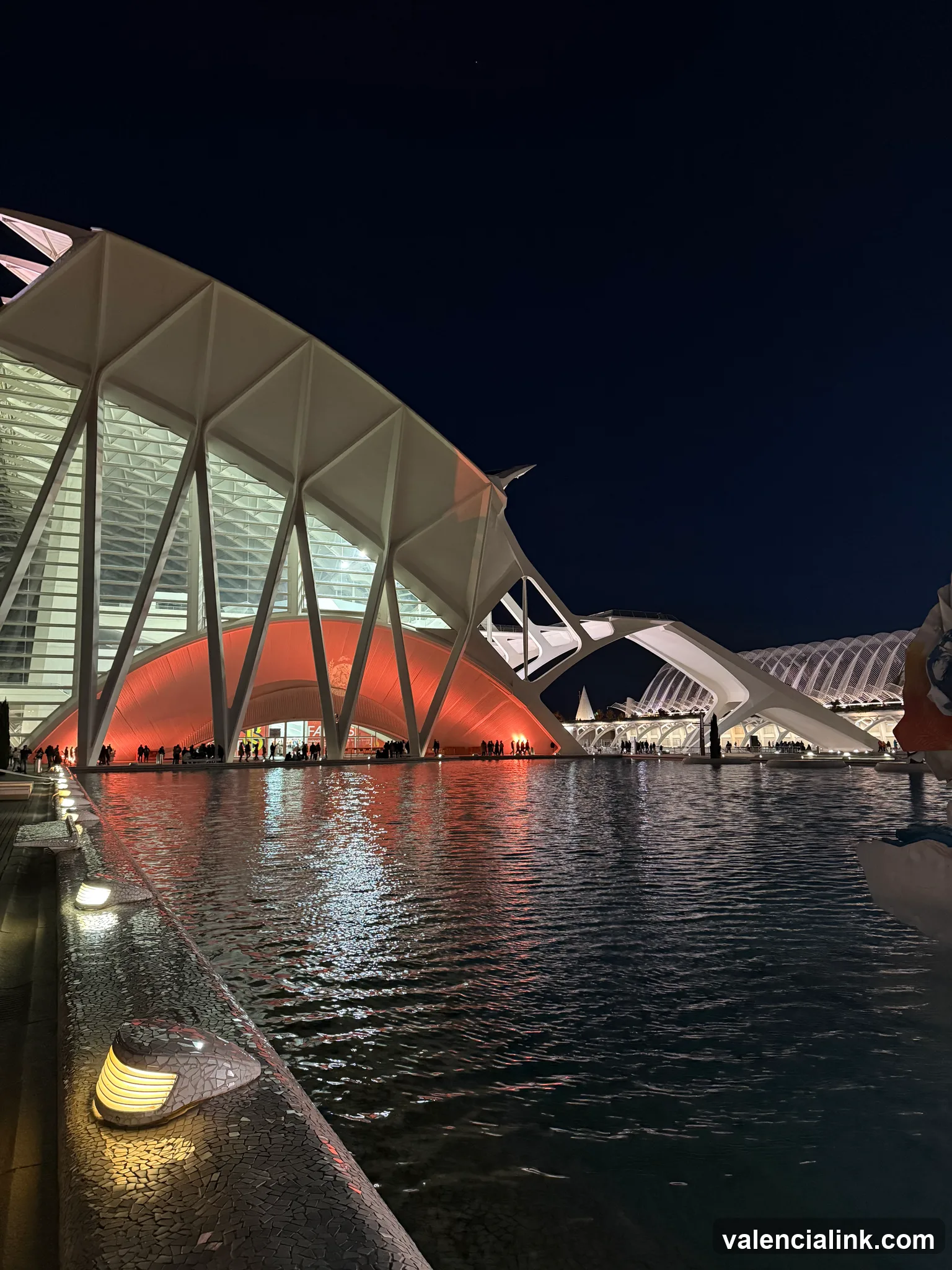 Modern architecture illuminated at night, reflected in water.