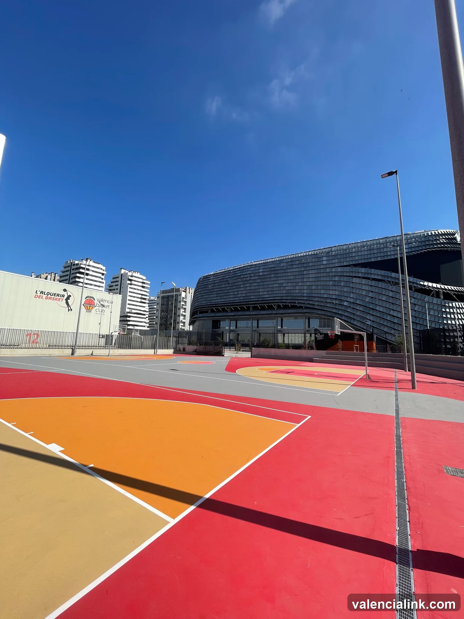 A vibrant basketball court with a modern architectural structure in the background and a clear blue sky above.