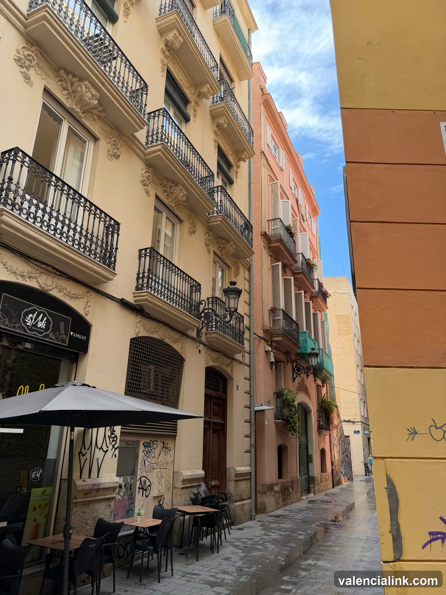 Narrow street with pastel buildings, balconies, and outdoor seating.